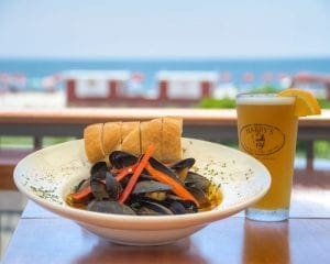 Image of clams in bowl with glass of beer on table.